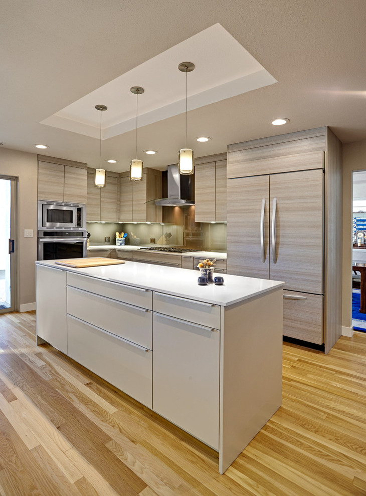 Geschlossene Moderne Küche mit flächenbündigen Schrankfronten, hellen Holzschränken, Glasrückwand, Elektrogeräten mit Frontblende, Quarzwerkstein-Arbeitsplatte und Küchenrückwand in Grün in Sacramento