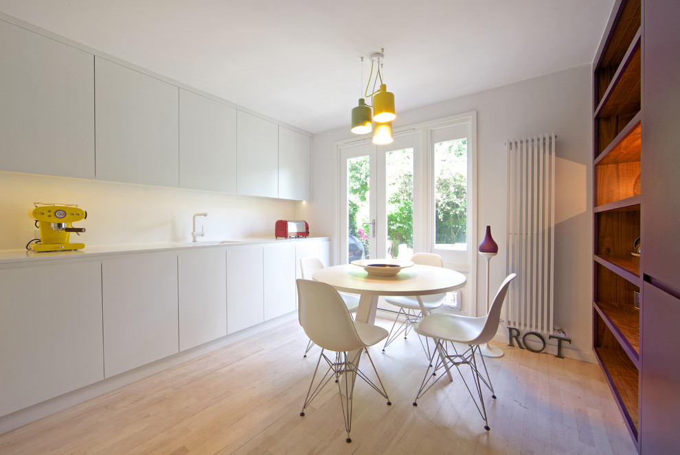 This is an example of a contemporary kitchen/diner in London with flat-panel cabinets, white cabinets and light hardwood flooring.
