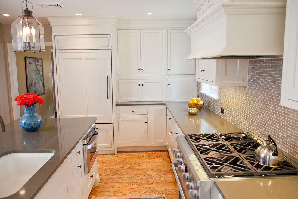 Klassisk inredning av ett mellanstort kök, med en undermonterad diskho, skåp i shakerstil, vita skåp, bänkskiva i kvarts, brunt stänkskydd, stänkskydd i tunnelbanekakel, rostfria vitvaror, mellanmörkt trägolv och en köksö
