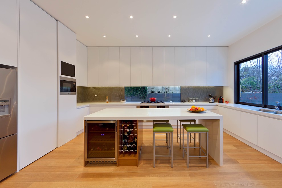 Moderne Küche in L-Form mit Unterbauwaschbecken, flächenbündigen Schrankfronten, weißen Schränken, Küchengeräten aus Edelstahl, braunem Holzboden und Kücheninsel in Melbourne