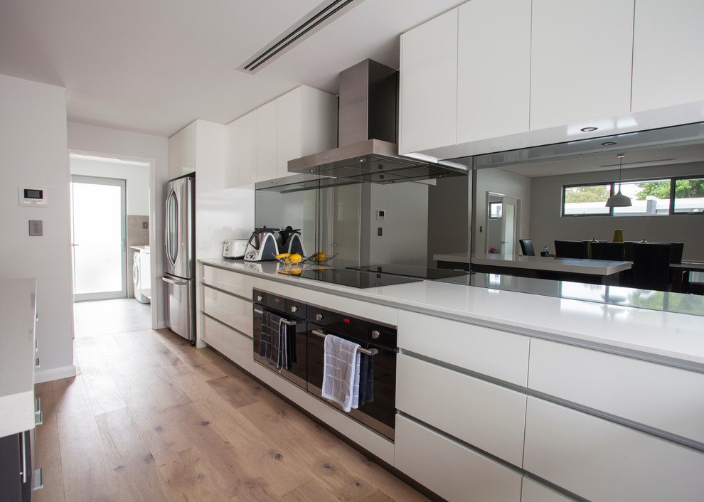 Offene Moderne Küche in L-Form mit flächenbündigen Schrankfronten, weißen Schränken, Mineralwerkstoff-Arbeitsplatte, hellem Holzboden, Kücheninsel und beigem Boden in Perth