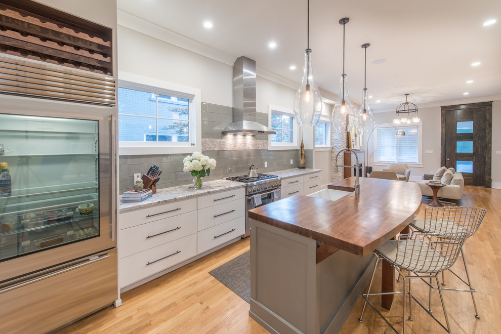 Design ideas for a traditional galley kitchen in Atlanta with a belfast sink, flat-panel cabinets, white cabinets, wood worktops, grey splashback, stainless steel appliances, medium hardwood flooring, an island, brown floors and brown worktops.