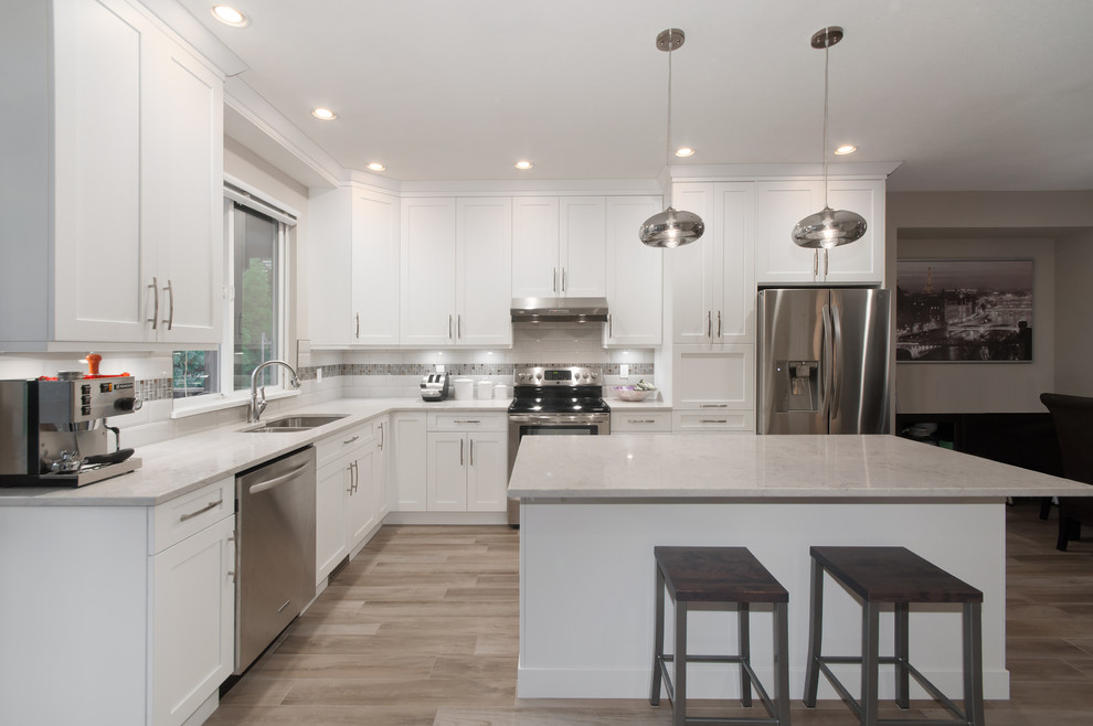 Inspiration for a mid-sized transitional l-shaped light wood floor eat-in kitchen remodel in Vancouver with an undermount sink, shaker cabinets, white cabinets, quartz countertops, white backsplash, ceramic backsplash, stainless steel appliances and an island