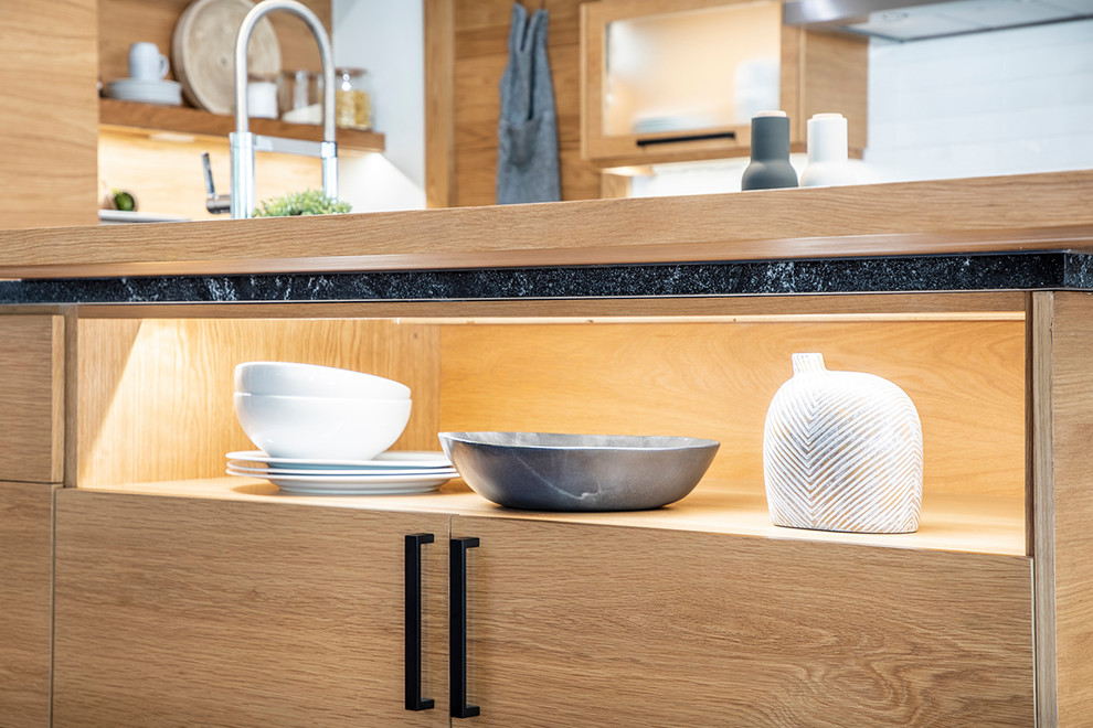 Modelo de cocinas en L escandinava abierta con puertas de armario de madera clara, salpicadero blanco, electrodomésticos de acero inoxidable, suelo de madera oscura, una isla y encimeras negras