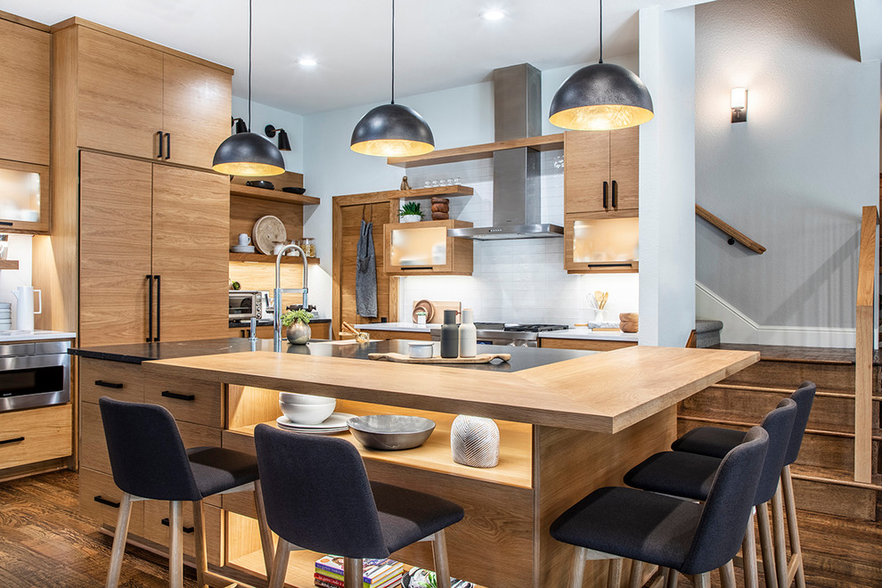 Example of a danish l-shaped dark wood floor open concept kitchen design in Dallas with light wood cabinets, white backsplash, stainless steel appliances, an island and black countertops