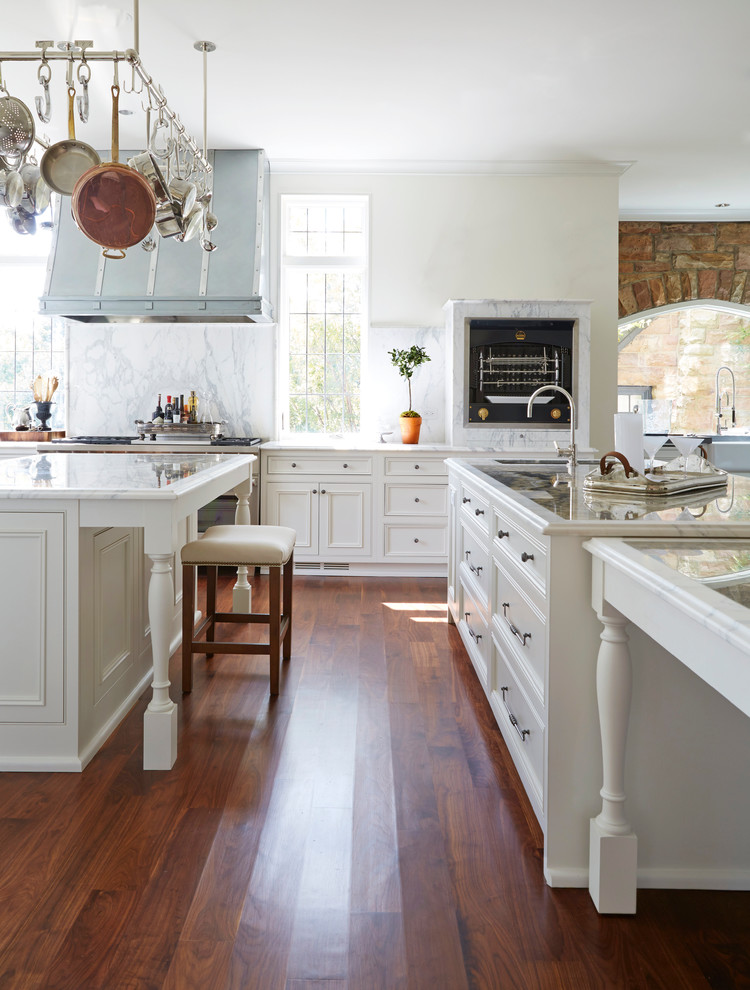 Design ideas for a large traditional kitchen/diner in Birmingham with a belfast sink, beaded cabinets, white cabinets, marble worktops, yellow splashback, stone slab splashback, stainless steel appliances, dark hardwood flooring and multiple islands.