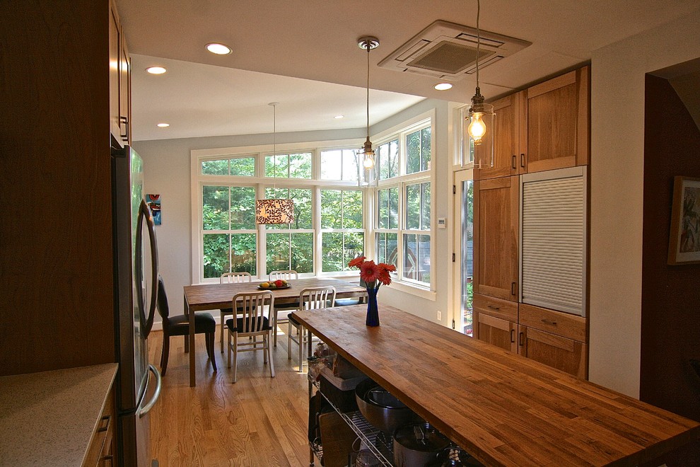 Foto på ett mellanstort funkis kök, med en undermonterad diskho, luckor med infälld panel, skåp i mellenmörkt trä, bänkskiva i återvunnet glas, grönt stänkskydd, stänkskydd i glaskakel, rostfria vitvaror, mellanmörkt trägolv och en köksö