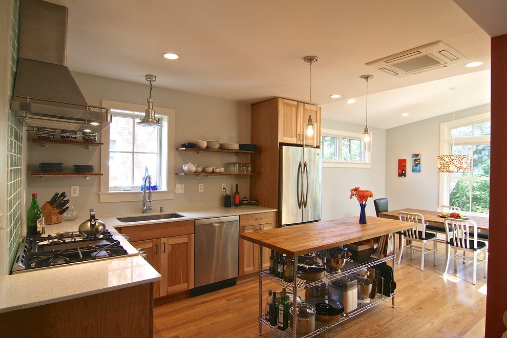 Bild på ett mellanstort funkis kök, med en undermonterad diskho, luckor med infälld panel, skåp i mellenmörkt trä, bänkskiva i återvunnet glas, grönt stänkskydd, stänkskydd i glaskakel, rostfria vitvaror, mellanmörkt trägolv och en köksö