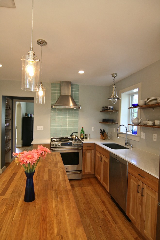 Inredning av ett modernt mellanstort kök, med en undermonterad diskho, luckor med infälld panel, skåp i mellenmörkt trä, bänkskiva i återvunnet glas, grönt stänkskydd, stänkskydd i glaskakel, rostfria vitvaror, mellanmörkt trägolv och en köksö