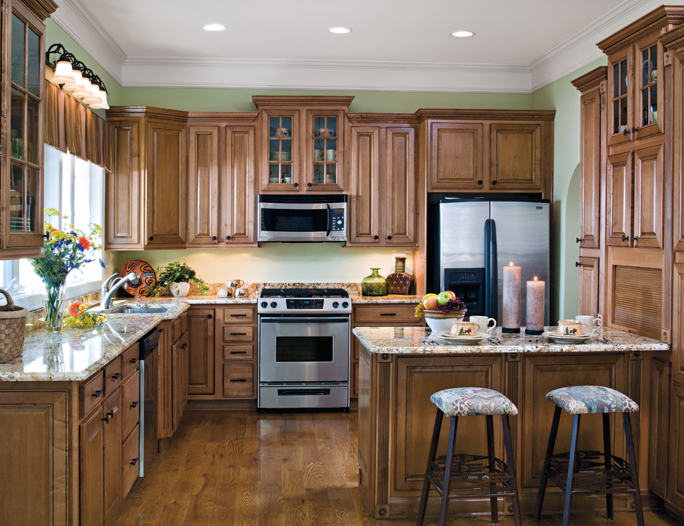 Inspiration for a large timeless l-shaped medium tone wood floor eat-in kitchen remodel in Indianapolis with an undermount sink, raised-panel cabinets, dark wood cabinets, granite countertops, beige backsplash, stainless steel appliances and a peninsula