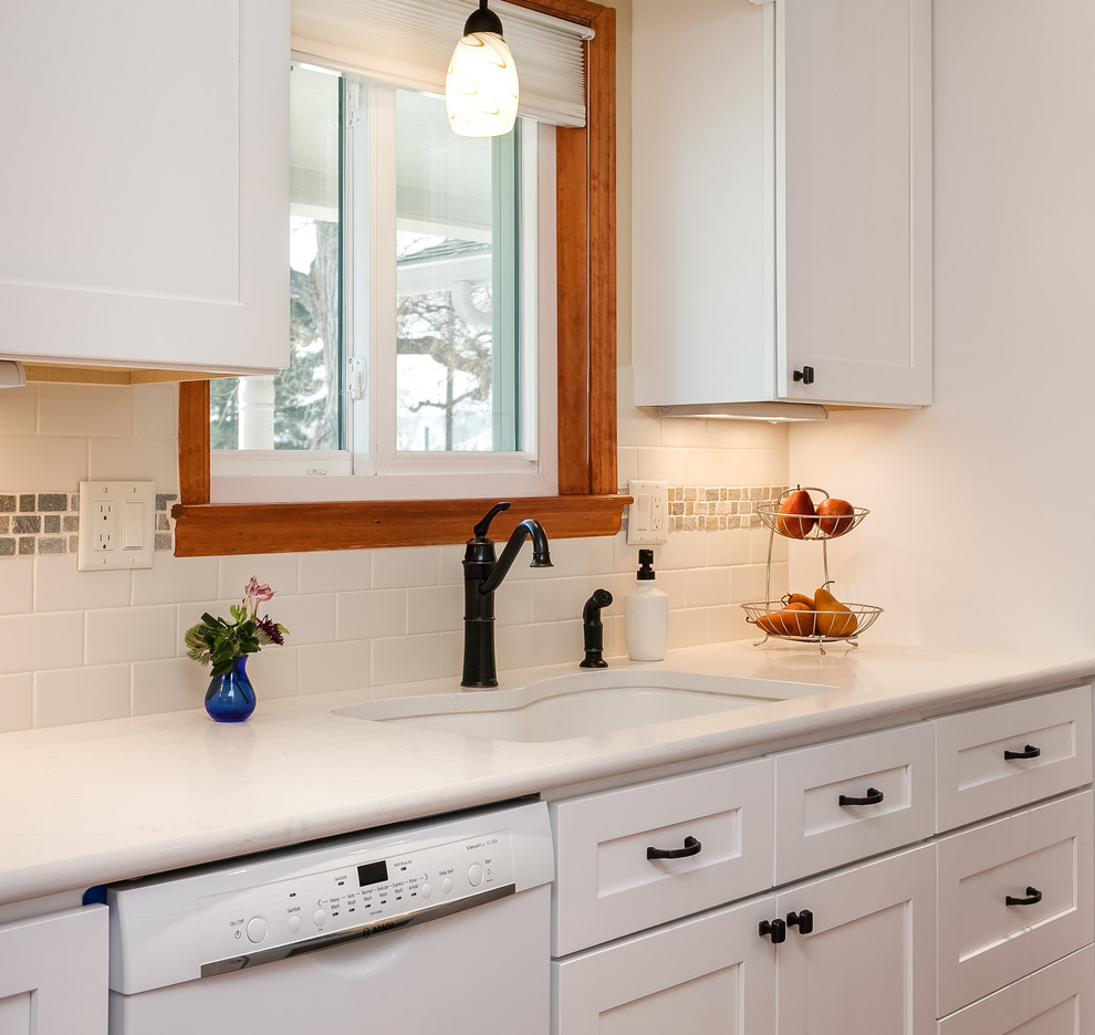This is an example of a medium sized classic galley kitchen/diner in Denver with a submerged sink, recessed-panel cabinets, white cabinets, composite countertops, white splashback, ceramic splashback, white appliances and medium hardwood flooring.