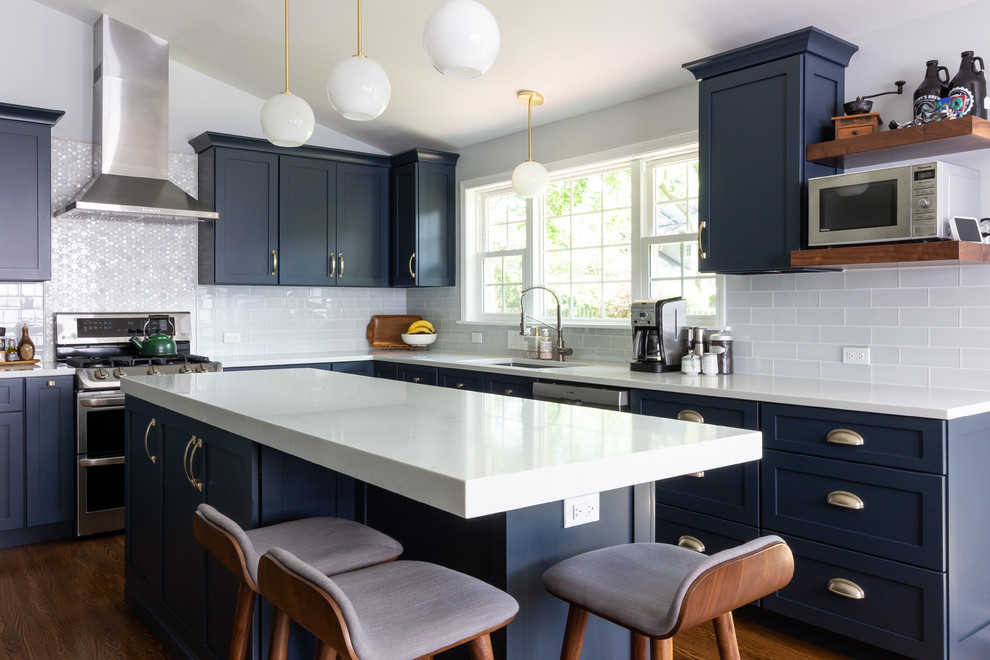 Klassische Küche in L-Form mit Unterbauwaschbecken, Schrankfronten im Shaker-Stil, blauen Schränken, Quarzwerkstein-Arbeitsplatte, Küchengeräten aus Edelstahl, Kücheninsel, weißer Arbeitsplatte, Küchenrückwand in Weiß, Rückwand aus Metrofliesen und braunem Holzboden in Boston