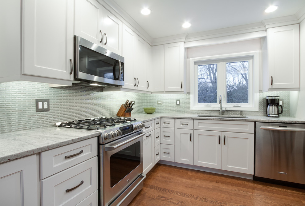 Photo of a classic kitchen in Chicago with a submerged sink, recessed-panel cabinets, white cabinets, granite worktops, grey splashback, ceramic splashback, stainless steel appliances and medium hardwood flooring.