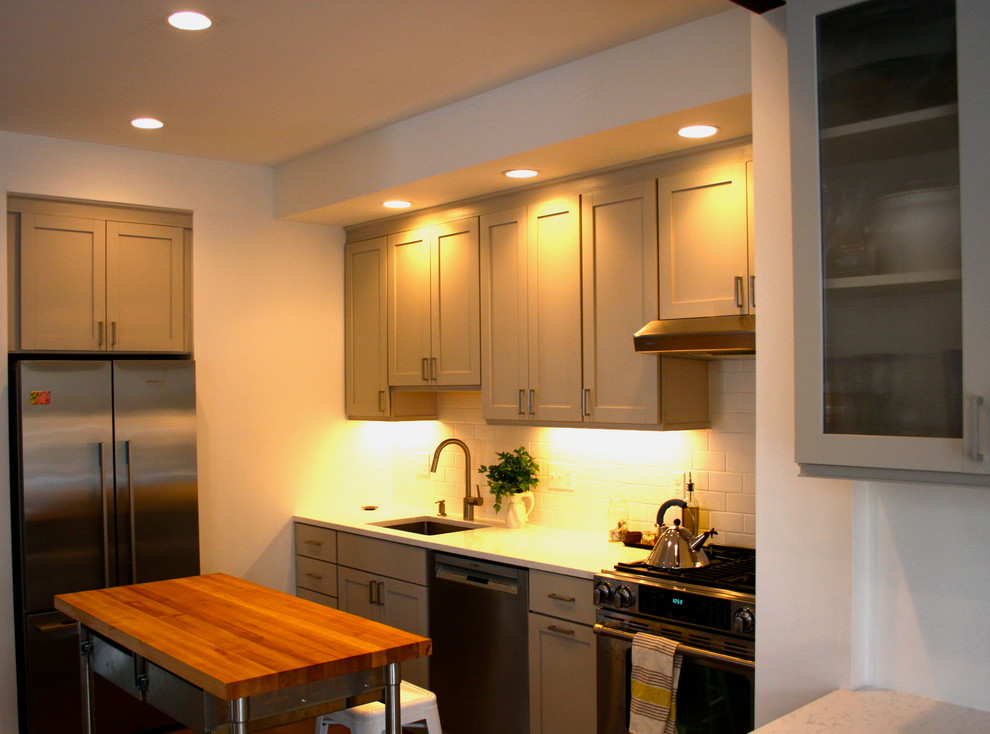 Exempel på ett litet klassiskt u-kök, med en undermonterad diskho, luckor med infälld panel, beige skåp, bänkskiva i kvarts, vitt stänkskydd, stänkskydd i tunnelbanekakel, rostfria vitvaror och en köksö