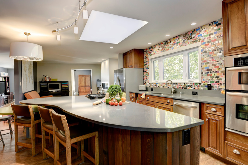 Mid-sized trendy single-wall medium tone wood floor eat-in kitchen photo in DC Metro with an undermount sink, raised-panel cabinets, medium tone wood cabinets, quartz countertops, multicolored backsplash, stainless steel appliances and two islands