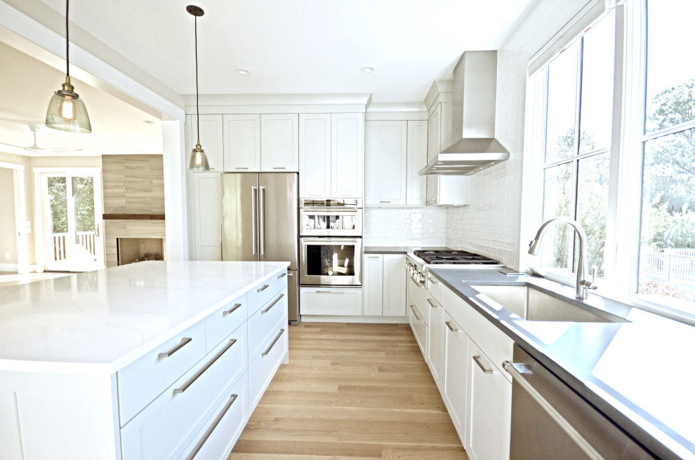 Inredning av ett modernt mellanstort vit vitt kök, med en undermonterad diskho, skåp i shakerstil, vita skåp, bänkskiva i kvartsit, vitt stänkskydd, stänkskydd i keramik, rostfria vitvaror, laminatgolv, en köksö och beiget golv