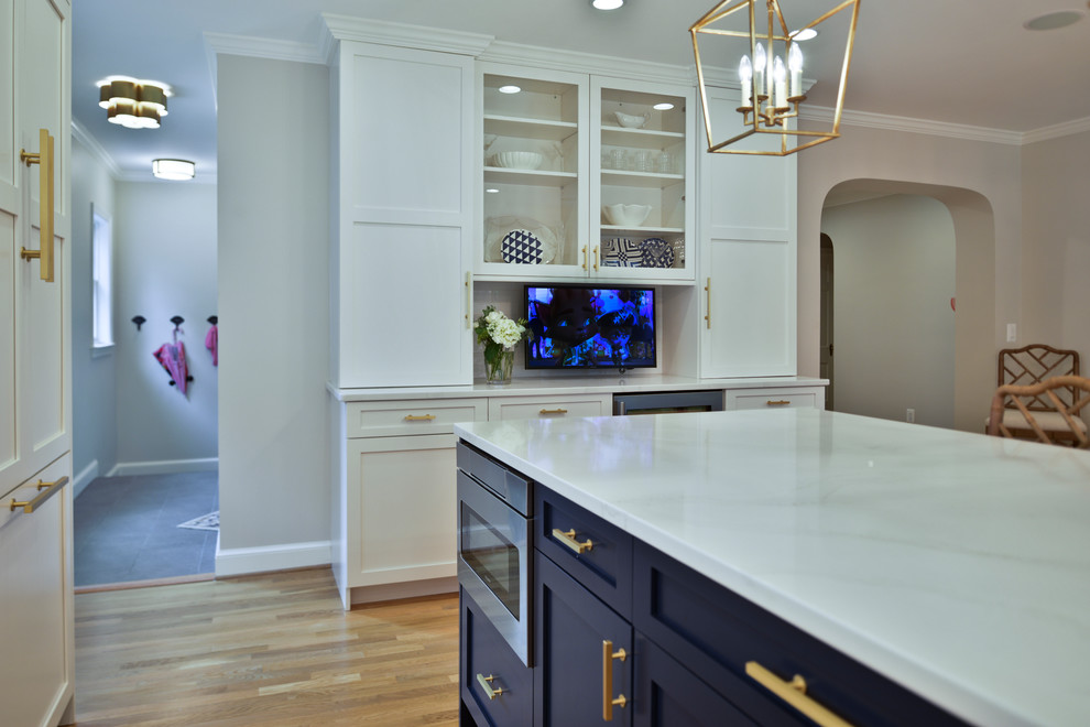 Photo of a medium sized traditional l-shaped kitchen/diner in DC Metro with a single-bowl sink, shaker cabinets, white cabinets, engineered stone countertops, white splashback, metro tiled splashback, integrated appliances, medium hardwood flooring, an island, brown floors and white worktops.