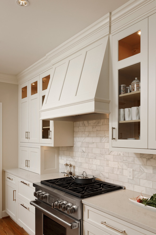 Klassisk inredning av ett litet kök, med vita skåp, en undermonterad diskho, luckor med infälld panel, bänkskiva i kalksten, stänkskydd i stenkakel, integrerade vitvaror, mellanmörkt trägolv, vitt stänkskydd och beiget golv