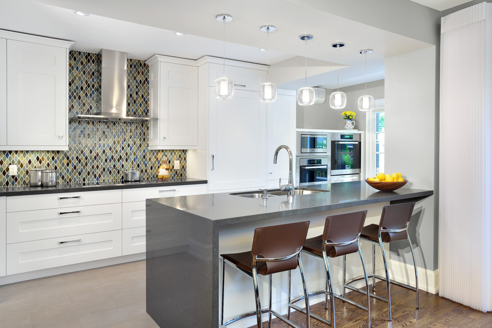 This is an example of a traditional galley kitchen in Toronto with a double-bowl sink, shaker cabinets, white cabinets, multi-coloured splashback and integrated appliances.