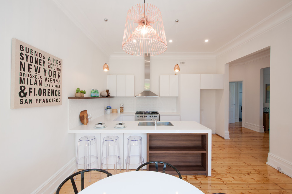 Inspiration for a medium sized contemporary u-shaped kitchen/diner in Melbourne with a double-bowl sink, flat-panel cabinets, white cabinets, engineered stone countertops, white splashback, metro tiled splashback, stainless steel appliances, light hardwood flooring and a breakfast bar.