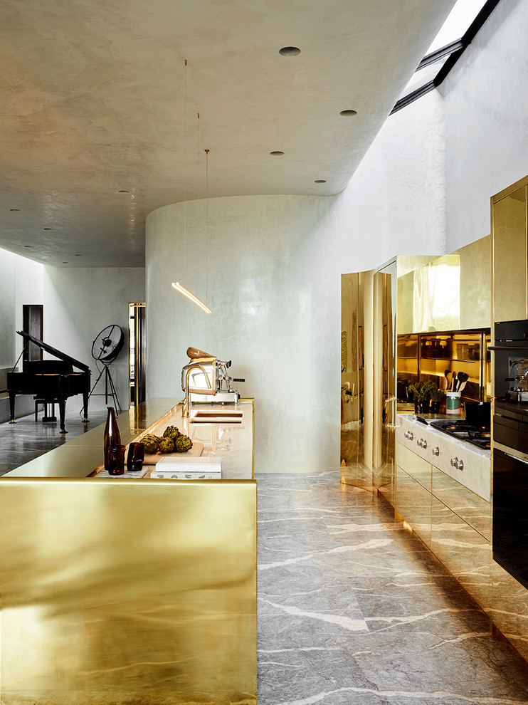 На фото: параллельная кухня-гостиная в современном стиле с врезной мойкой, плоскими фасадами, желтыми фасадами, фартуком цвета металлик, фартуком из металлической плитки, черной техникой, островом и серым полом с