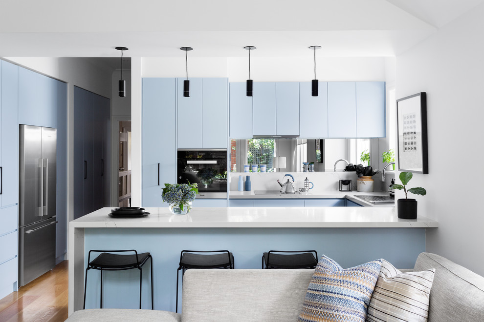 Foto på ett funkis kök, med en nedsänkt diskho, släta luckor, blå skåp, stänkskydd med metallisk yta, spegel som stänkskydd, rostfria vitvaror, ljust trägolv, en halv köksö och brunt golv