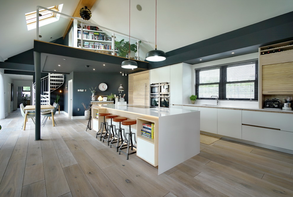 This is an example of a large contemporary single-wall open plan kitchen in Other with a submerged sink, flat-panel cabinets, white cabinets, light hardwood flooring, an island, beige floors and white splashback.