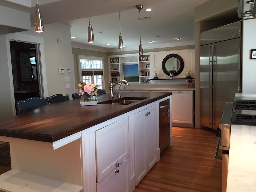 This is an example of a large contemporary l-shaped kitchen/diner in Denver with a submerged sink, raised-panel cabinets, white cabinets, wood worktops, white splashback, stainless steel appliances, light hardwood flooring, an island, multi-coloured floors and brown worktops.