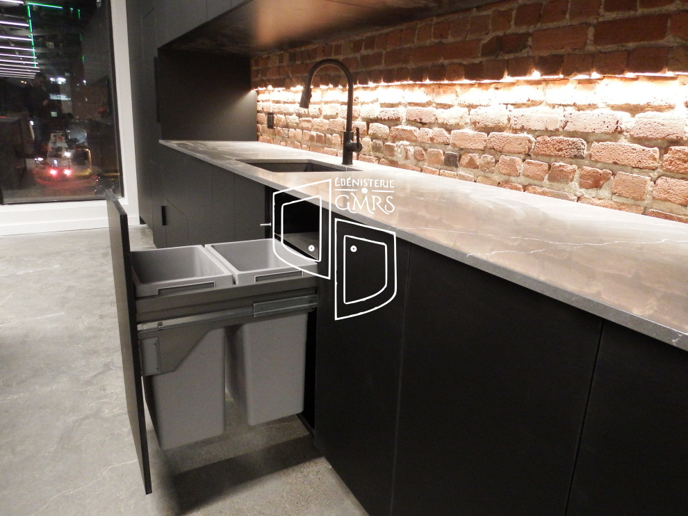 Large minimalist single-wall concrete floor, gray floor and exposed beam eat-in kitchen photo in Montreal with an undermount sink, flat-panel cabinets, black cabinets, quartz countertops, red backsplash, brick backsplash, paneled appliances, an island and gray countertops