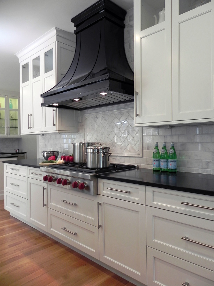 Klassisk inredning av ett stort kök, med en undermonterad diskho, skåp i shakerstil, vita skåp, marmorbänkskiva, vitt stänkskydd, stänkskydd i stenkakel, rostfria vitvaror, mellanmörkt trägolv, en köksö och brunt golv