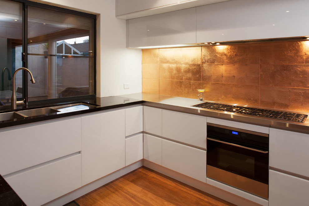 Mittelgroße Moderne Wohnküche in L-Form mit Unterbauwaschbecken, weißen Schränken, Granit-Arbeitsplatte, Küchenrückwand in Metallic, Rückwand aus Glasfliesen, Küchengeräten aus Edelstahl, braunem Holzboden und Kücheninsel in Perth