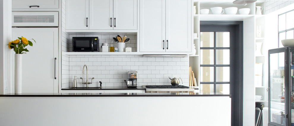 Example of a small urban u-shaped medium tone wood floor eat-in kitchen design in New York with an undermount sink, recessed-panel cabinets, white cabinets, quartz countertops, white backsplash, ceramic backsplash, paneled appliances and a peninsula