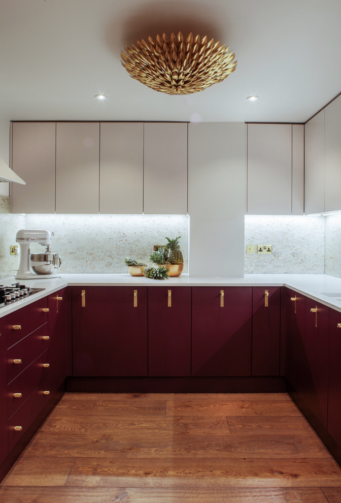 This is an example of a contemporary u-shaped enclosed kitchen in London with a built-in sink, flat-panel cabinets, red cabinets, composite countertops, metallic splashback, stainless steel appliances, medium hardwood flooring, no island and brown floors.