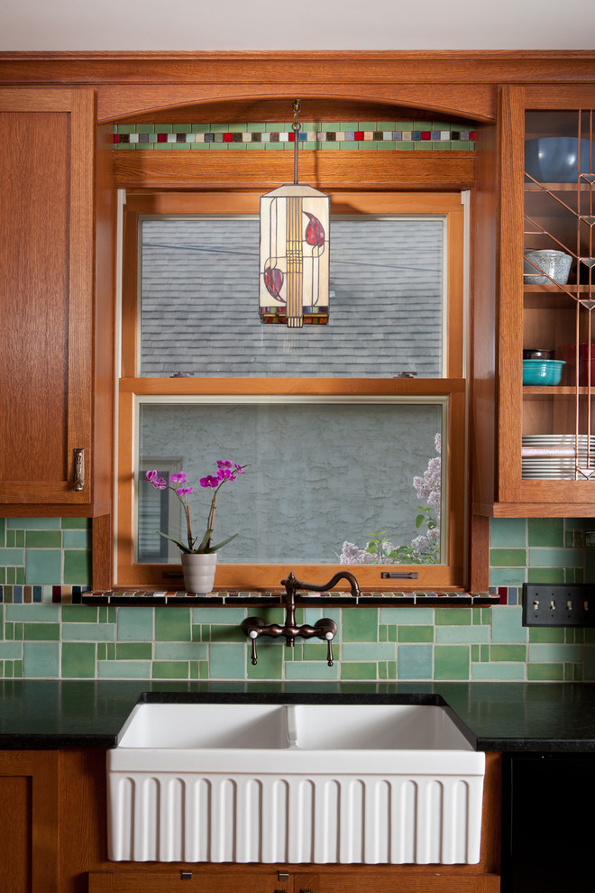 Example of a small classic u-shaped enclosed kitchen design in Minneapolis with a farmhouse sink, shaker cabinets, dark wood cabinets, solid surface countertops, green backsplash, cement tile backsplash, black appliances and no island