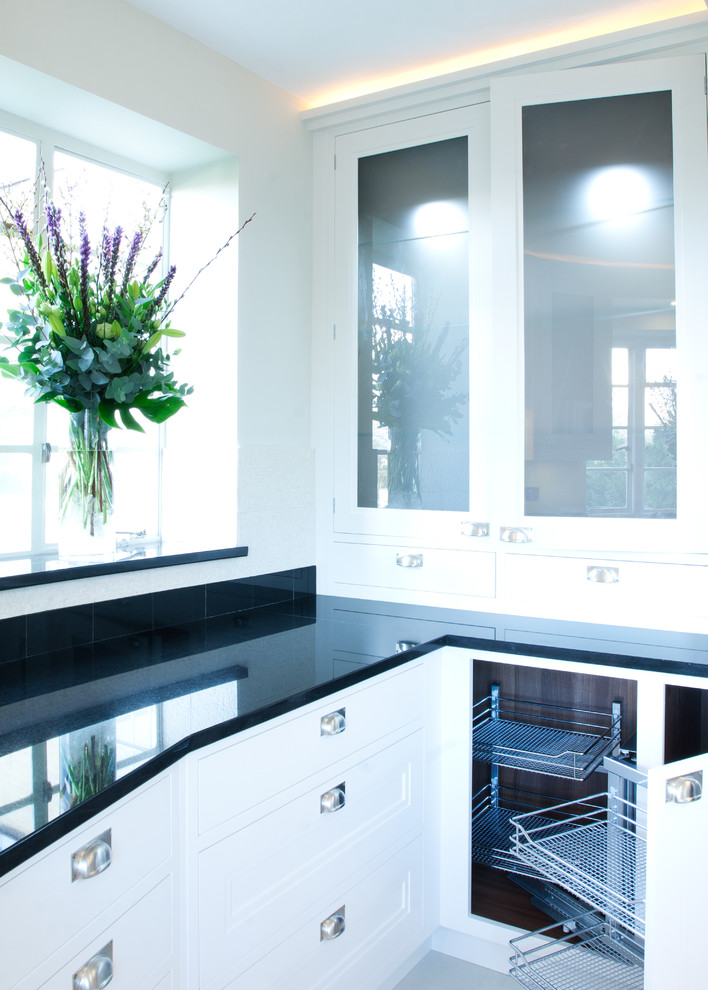 Immagine di una cucina chic chiusa e di medie dimensioni con lavello sottopiano, ante bianche, top in granito, elettrodomestici neri e pavimento in pietra calcarea