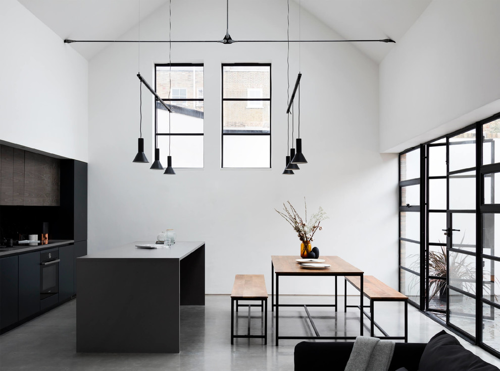 Cette photo montre une cuisine ouverte moderne avec un placard à porte plane, une crédence noire, un électroménager noir, sol en béton ciré, îlot, un sol gris et un plan de travail gris.