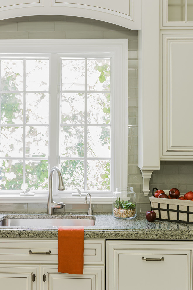 Mid-sized transitional l-shaped medium tone wood floor and brown floor kitchen photo in Boston with an undermount sink, raised-panel cabinets, white cabinets, granite countertops, green backsplash, glass tile backsplash, paneled appliances and an island