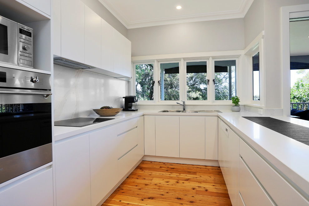 This is an example of a medium sized contemporary u-shaped open plan kitchen in Sydney with a built-in sink, flat-panel cabinets, white cabinets, engineered stone countertops, white splashback, stone slab splashback, stainless steel appliances, medium hardwood flooring, a breakfast bar, yellow floors and white worktops.