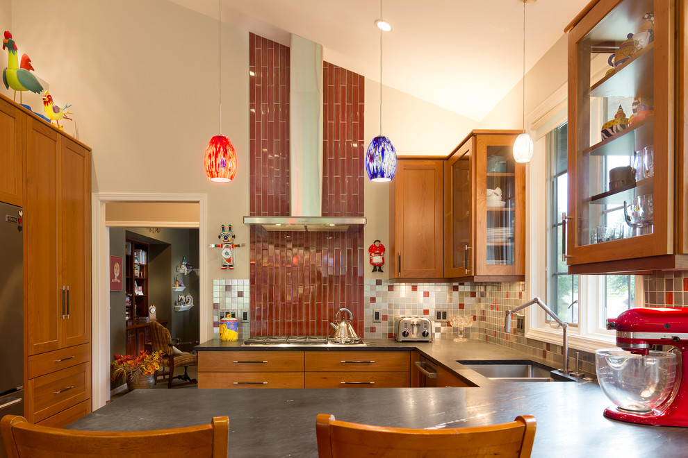 Foto på ett mellanstort eklektiskt kök, med en undermonterad diskho, luckor med infälld panel, skåp i mellenmörkt trä, bänkskiva i täljsten, stänkskydd med metallisk yta, stänkskydd i metallkakel, rostfria vitvaror, mellanmörkt trägolv och en halv köksö