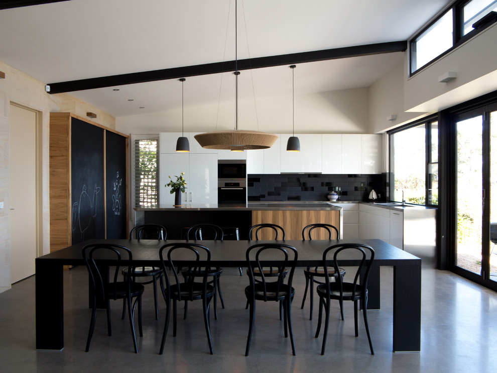 Стильный дизайн: кухня в современном стиле с черным фартуком, обеденным столом и черно-белыми фасадами - последний тренд