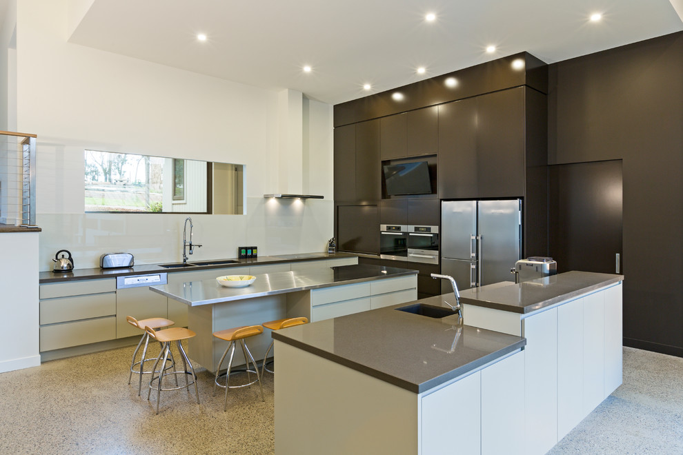 Contemporary kitchen pantry in Melbourne with a double-bowl sink, stainless steel worktops, concrete flooring and multiple islands.