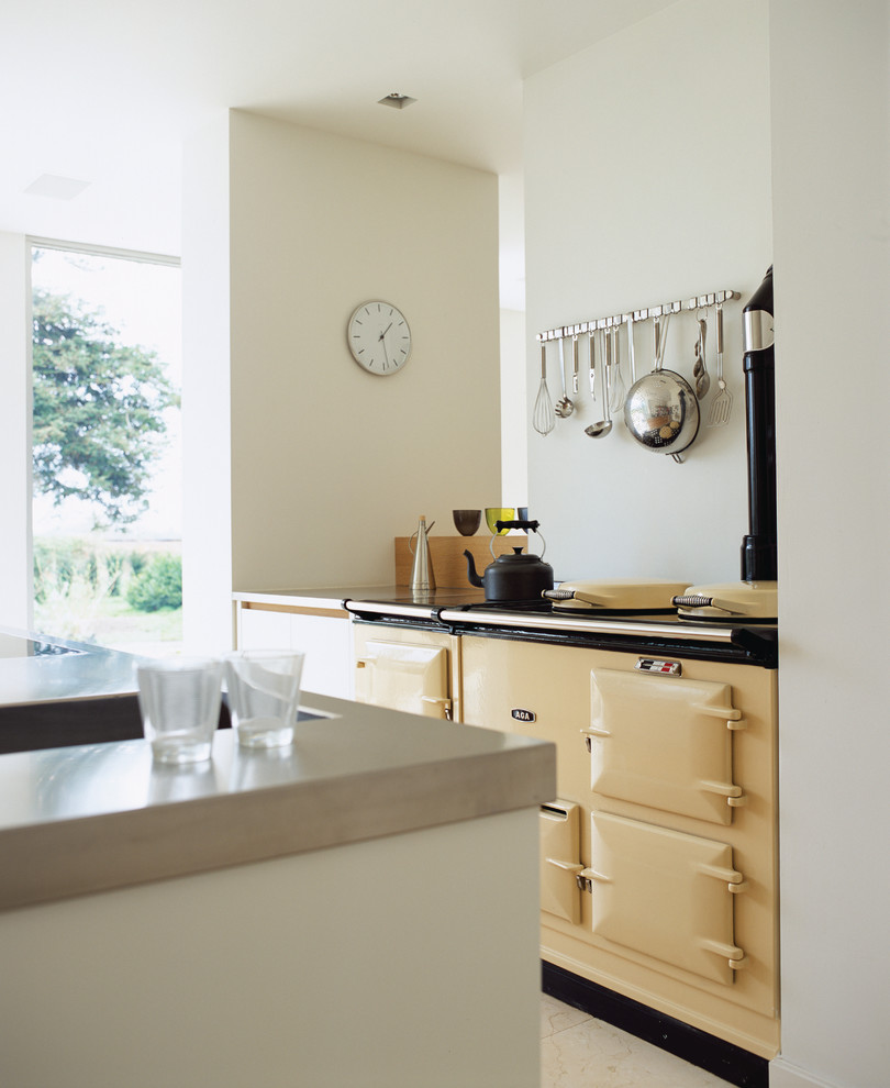 Offene, Mittelgroße Moderne Küche mit flächenbündigen Schrankfronten, weißen Schränken, Edelstahl-Arbeitsplatte, Glasrückwand, Kücheninsel, integriertem Waschbecken, Küchengeräten aus Edelstahl und grauer Arbeitsplatte in Hertfordshire