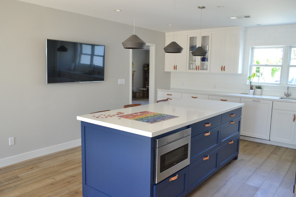 Large farmhouse l-shaped kitchen/diner in San Francisco with a submerged sink, shaker cabinets, blue cabinets, engineered stone countertops, white splashback, metro tiled splashback, stainless steel appliances, light hardwood flooring, brown floors and white worktops.
