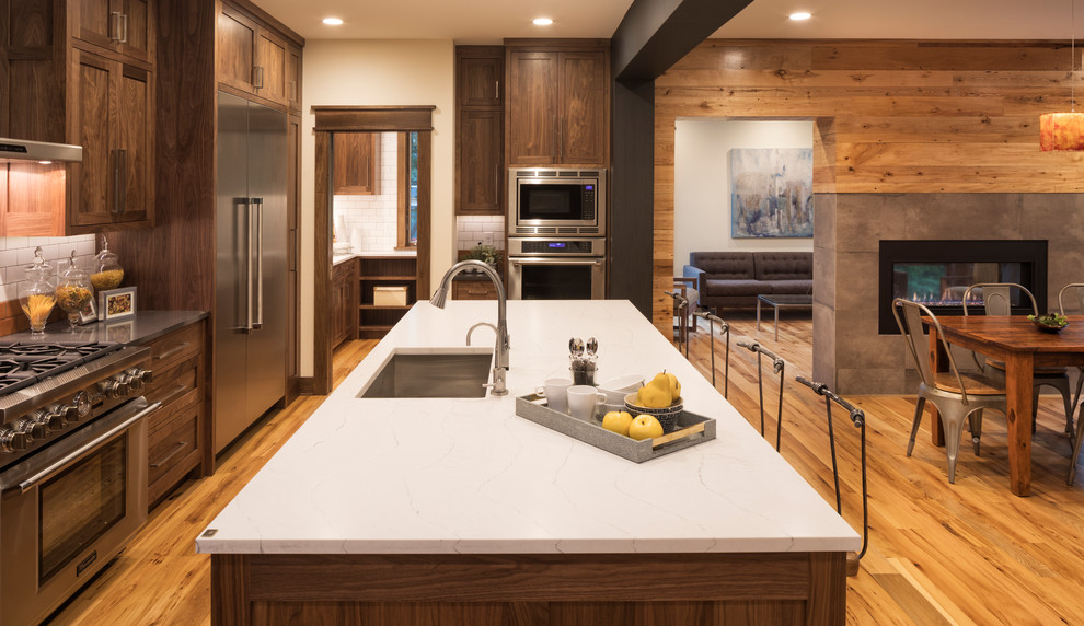 Eat-in kitchen - rustic single-wall medium tone wood floor eat-in kitchen idea in Minneapolis with an undermount sink, recessed-panel cabinets, dark wood cabinets, stainless steel appliances, an island and white backsplash