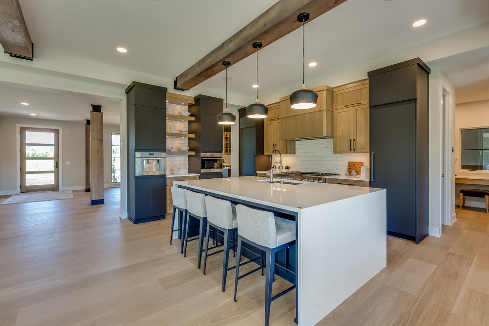 Large classic l-shaped kitchen/diner in Minneapolis with a submerged sink, flat-panel cabinets, black cabinets, engineered stone countertops, white splashback, porcelain splashback, stainless steel appliances, light hardwood flooring, an island, beige floors and white worktops.
