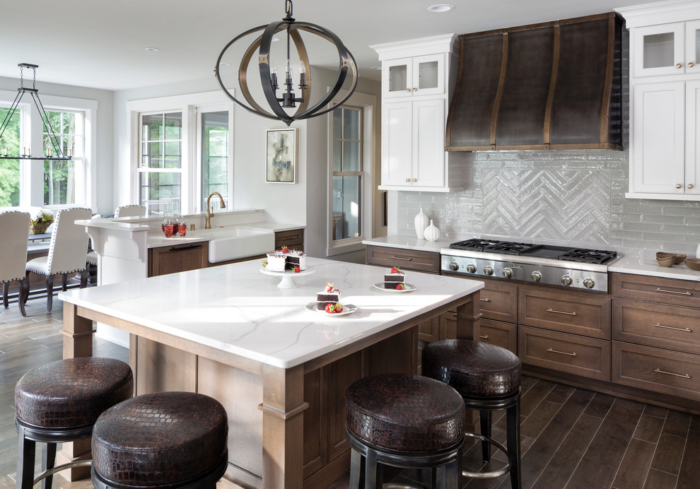 Example of a large transitional u-shaped dark wood floor and brown floor eat-in kitchen design in Minneapolis with a farmhouse sink, recessed-panel cabinets, brown cabinets, quartzite countertops, gray backsplash, glass tile backsplash, paneled appliances and an island