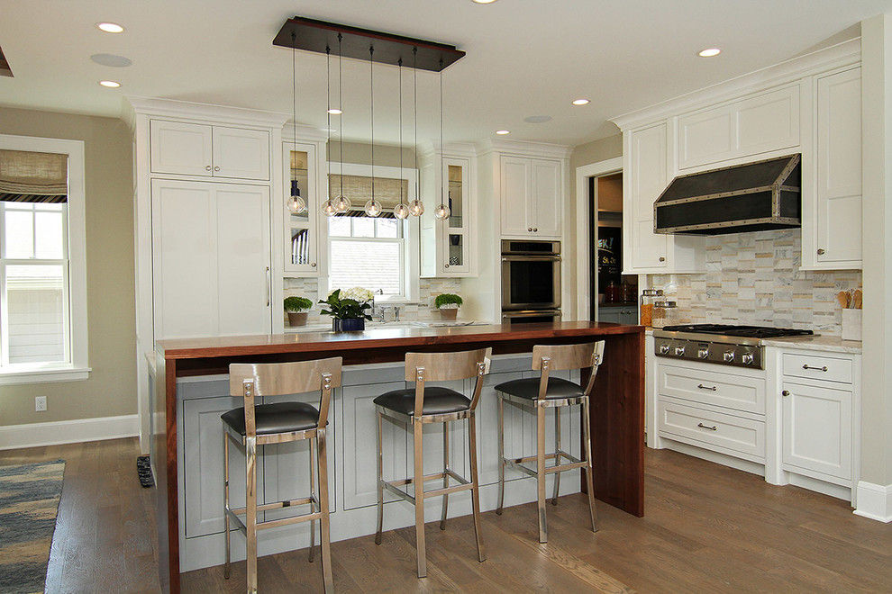 Klassische Küche in L-Form mit Schrankfronten im Shaker-Stil, weißen Schränken, Küchenrückwand in Beige, Elektrogeräten mit Frontblende, braunem Holzboden und Kücheninsel in Minneapolis