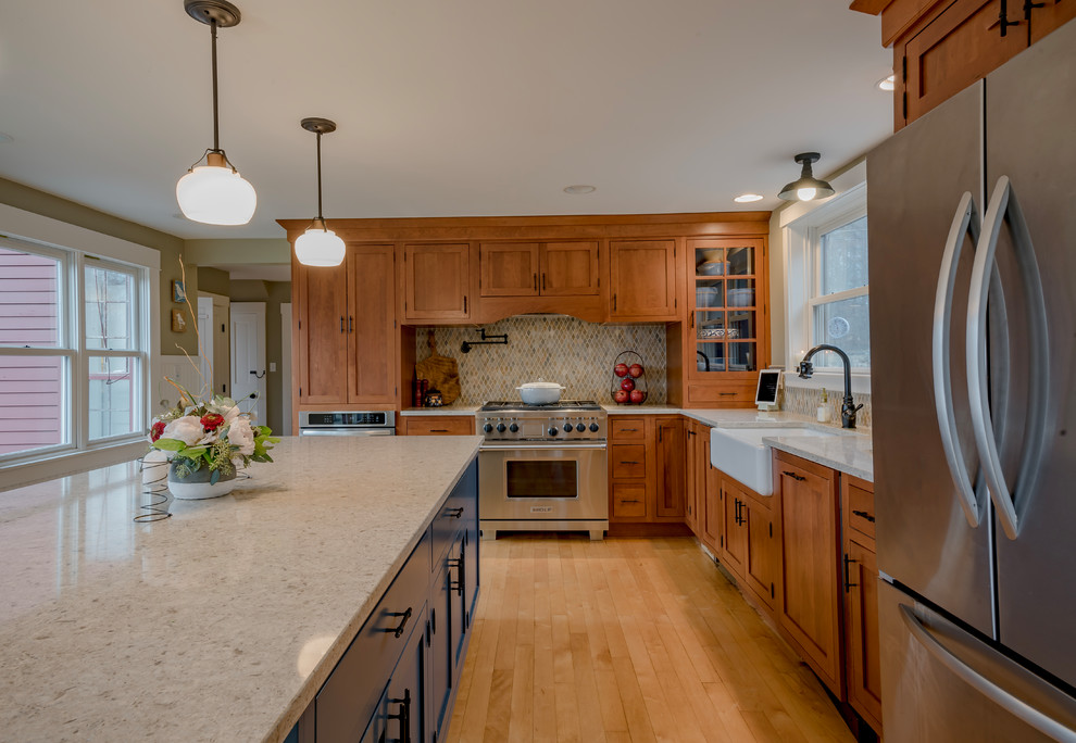 Example of a mid-sized country l-shaped light wood floor and brown floor eat-in kitchen design in Boston with a farmhouse sink, shaker cabinets, medium tone wood cabinets, quartz countertops, beige backsplash, mosaic tile backsplash, stainless steel appliances, an island and beige countertops