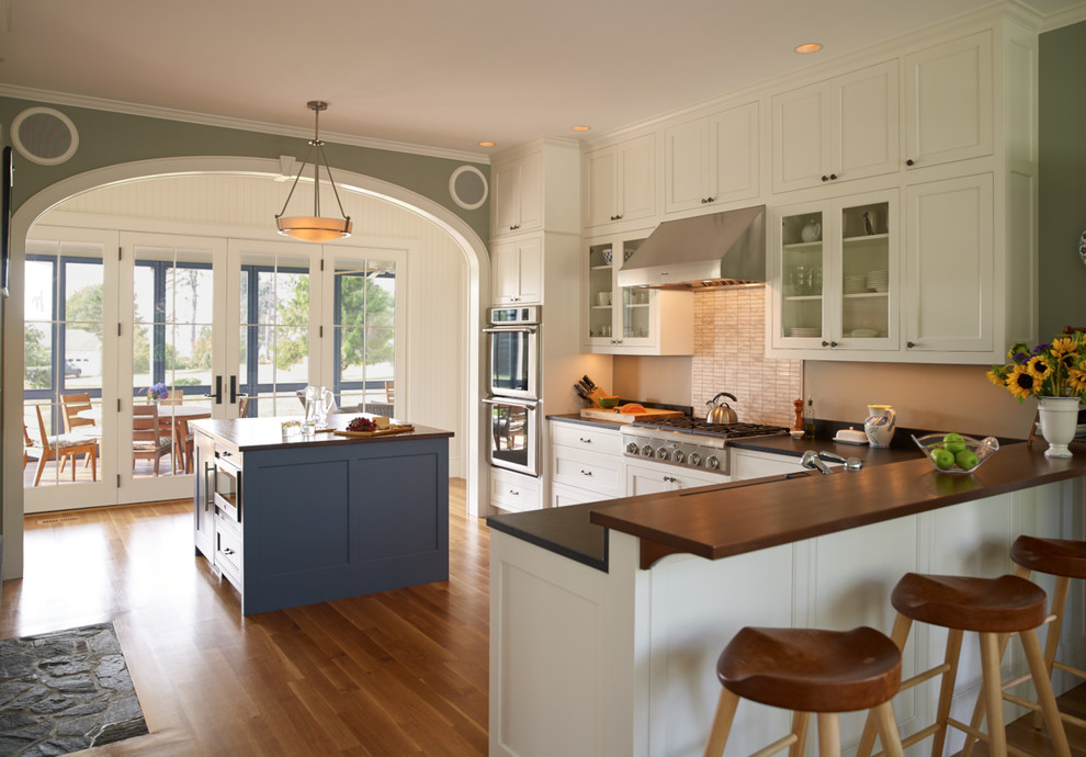 Maritime Küche in L-Form mit weißen Schränken, Küchenrückwand in Beige, braunem Holzboden, Kücheninsel, Schrankfronten im Shaker-Stil und Küchengeräten aus Edelstahl in Portland Maine