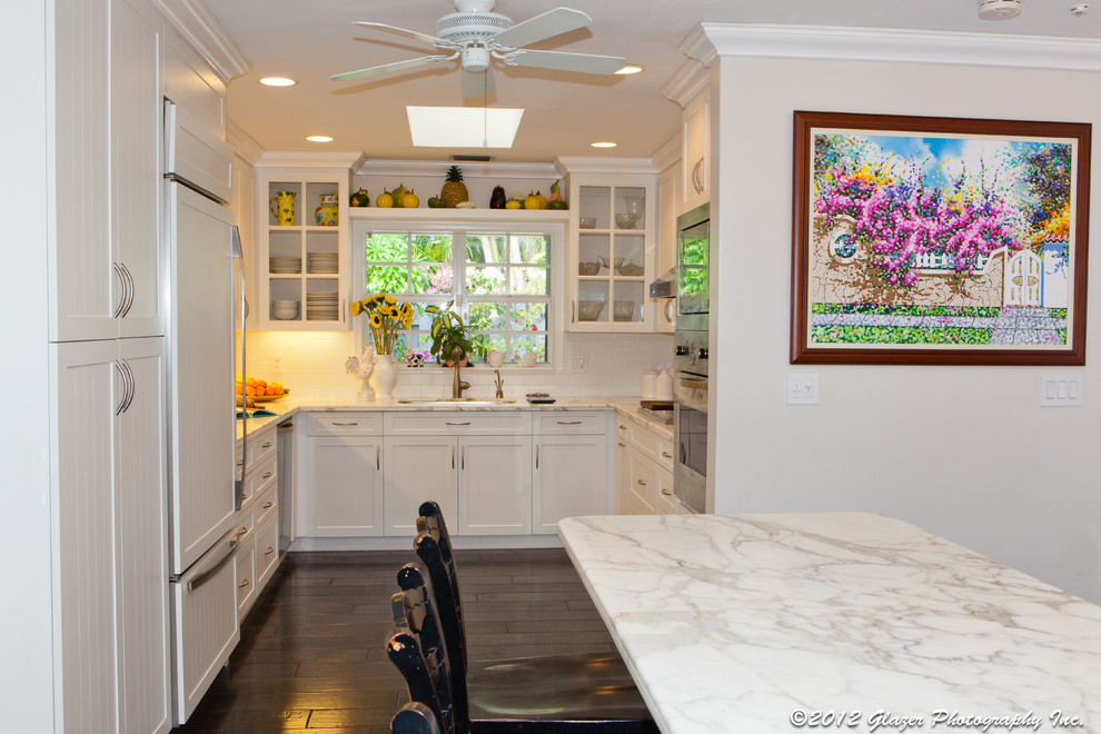 マイアミにあるエクレクティックスタイルのおしゃれなキッチン (アンダーカウンターシンク、ガラス扉のキャビネット、白いキャビネット、大理石カウンター、白いキッチンパネル、サブウェイタイルのキッチンパネル、シルバーの調理設備) の写真